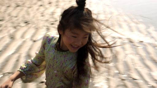 Ein Kind dreht sich mit wehenden Haaren am Strand