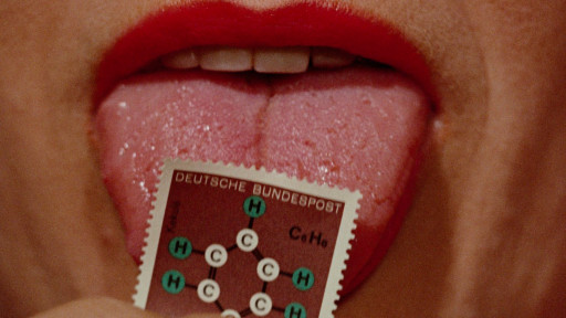 Eine Nahaufnahme eines Mundes mit rot geschminkten Lippen. Die Zunge leckt an einer Briefmarke, auf der ein chemisches Molekül abgebildet ist.