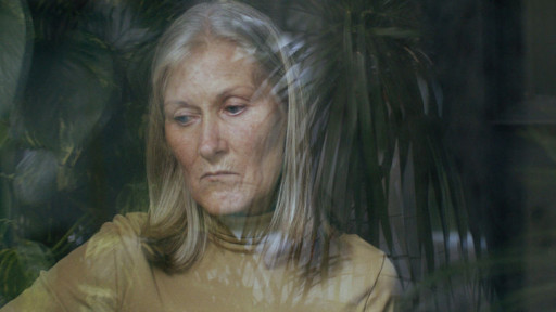 Eine ältere Frau schaut wehmütig aus einem Fenster.