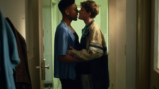 Zwei junge Männer küssen sich an der offenen Wohnungstür